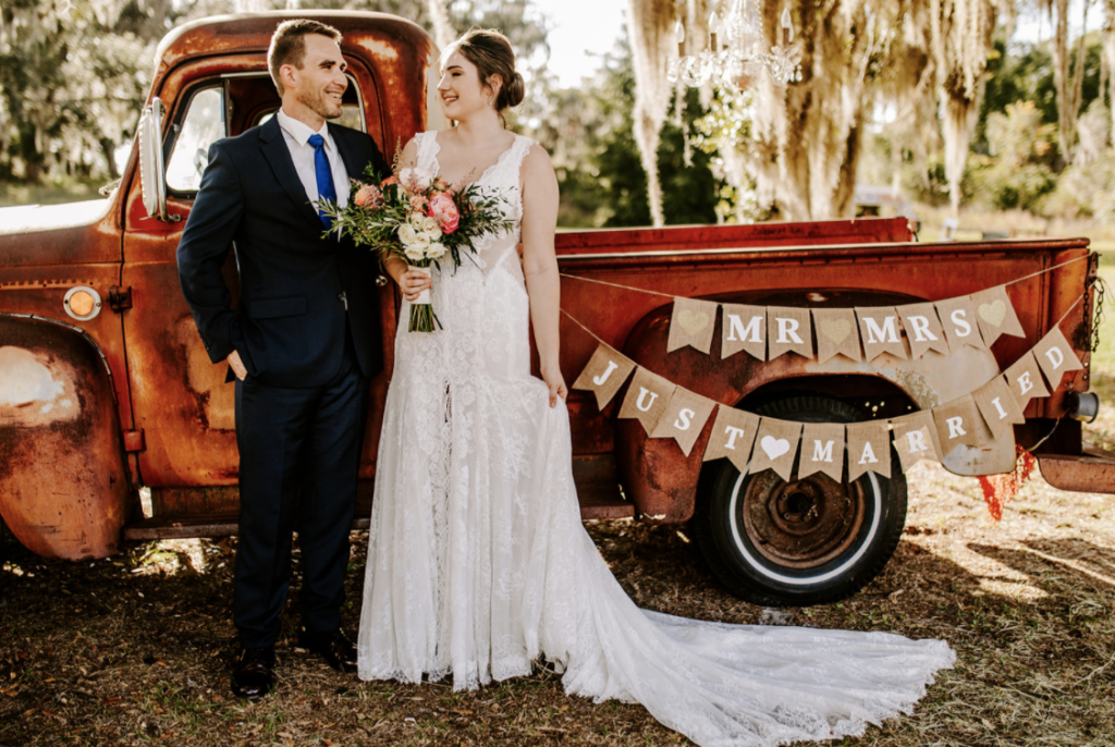 Couple standing beside a vintage red truck with a Just Married banner