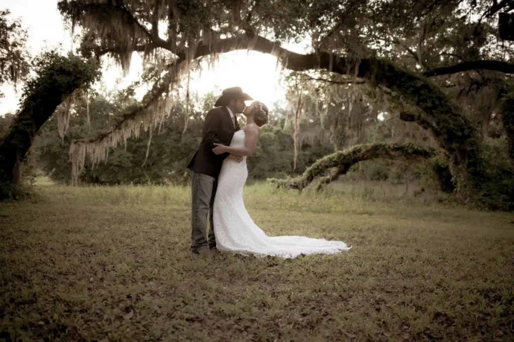 Bride and groom kissing under a large oak tree during an outdoor wedding ceremony