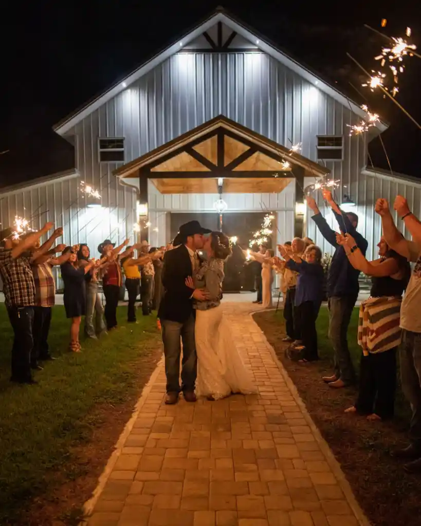 Bride and groom kissing on a brick pathway during a sparkler send-off at a outdoor wedding venue at night.