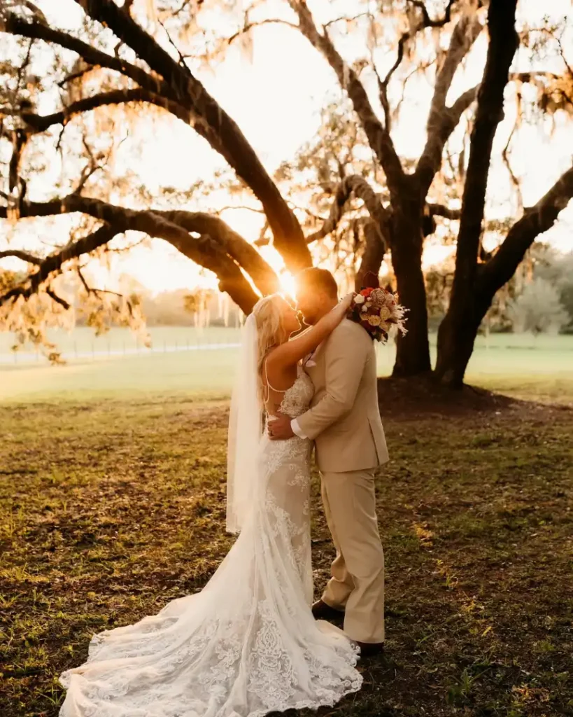 Bride and groom embracing outdoors under oak trees at sunset during a rustic Florida barn wedding at Legacy at Oak Meadows.