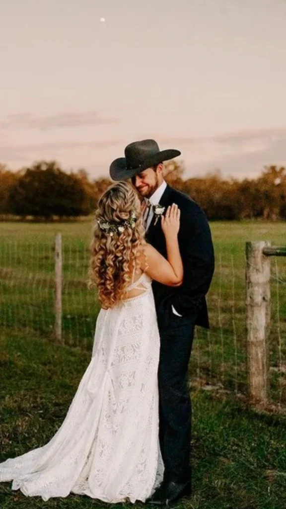 Couple embracing in a field at sunset, groom wearing a black cowboy hat