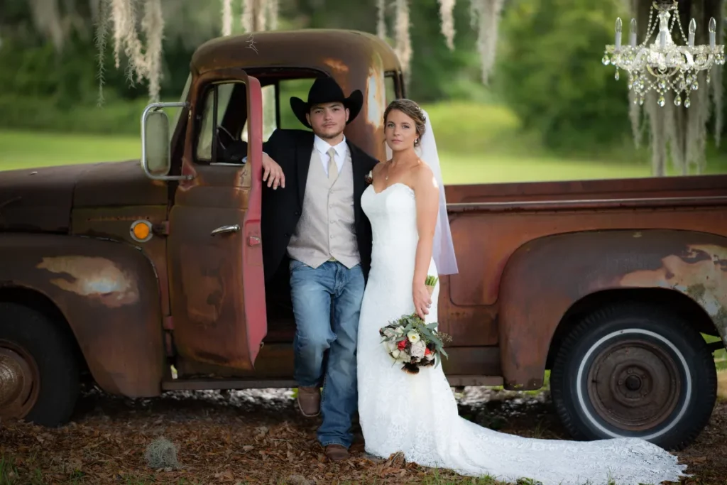 Groom leaning out of a vintage truck window beside the bride in a wooded setting