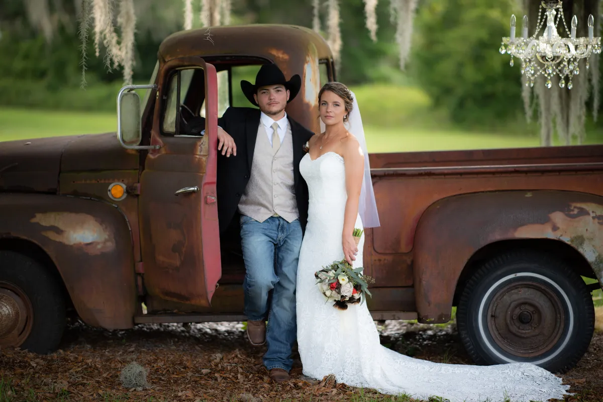 Groom leaning out of a vintage truck window beside the bride in a wooded setting